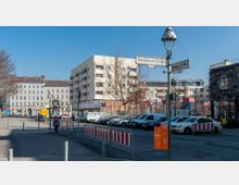 Städtische Straßenszene mit Wohngebäuden im Hintergrund, parkenden Autos und einem Mülleimer im Vordergrund. Ein Straßenschild zeigt die Kreuzung der Kurmärkischen Straße und der Frobenstraße, während im rechten Bildbereich ein umzäunter Spielplatz sichtbar ist.