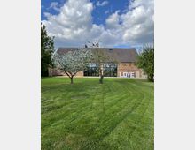 Ein Backsteingebäude mit großen Glasfenstern und spitzem Dach auf einer großen, gepflegten Rasenfläche, umgeben von blühenden Bäumen; an der rechten Gebäudeseite steht der Schriftzug „LOVE“.