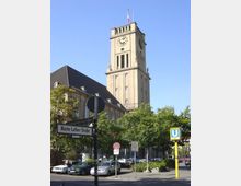 Hohes historisches Gebäude mit einem Turm und einer großen Uhr, umgeben von Bäumen und geparkten Autos; im Vordergrund Straßenschilder, darunter ein Schild mit der Aufschrift "Martin-Luther-Straße" und ein gelbes U-Bahn-Schild für die Linie U4.