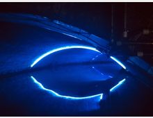 Eine dunkle Umgebung mit einer blauen, leuchtenden, halbkreisförmigen Lichtlinie, die sich in einer Wasseroberfläche spiegelt. Oben sind einige Rohre und Kabel sichtbar, die auf eine industrielle oder technische Umgebung hindeuten.