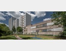 Mehrere große Wohnhochhäuser und ein flaches, graues Gebäude mit rechteckigen Fenstern stehen in einer grünen Umgebung. Ein befestigter Weg führt durch eine Wiese, Bäume säumen das Gelände, und eine Person mit Hund ist im Vordergrund zu sehen.