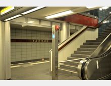 U-Bahn-Station mit der Beschilderung "Kleistpark". Sichtbar sind ein Treppenaufgang, eine Rolltreppe, Wandfliesen in Grau und Blau sowie ein Pfeiler mit einem blauen Tastknopf.