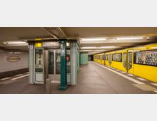 U-Bahn-Station Wittenbergplatz in Berlin mit gelbem Zug an einem der Bahnsteige. Die Station hat gekachelte Wände, grüne Säulen und gut beleuchtete Decken mit Hinweisschildern für die Linien U2 und U3.
