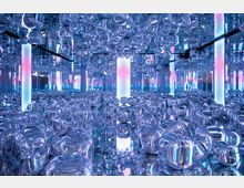 Ein futuristischer Raum mit spiegelnden Wänden, glänzenden, durchsichtigen Kugeln auf Boden und Decke sowie leuchtenden Säulen in blauem und pinkem Licht. Die reflektierenden Elemente erzeugen eine optische Illusion von Tiefe.