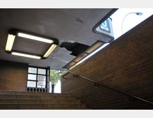 Treppenaufgang in einer U-Bahn-Unterführung mit Ziegelwänden und angeschlagenem Deckenelement. Leuchtstofflampen an der Decke und ein U7-Schild in der oberen rechten Bildhälfte, teilweise verdeckt von der Decke.