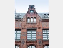 Backsteinfassade eines historischen Gebäudes mit der Aufschrift „SAROTTI“ an der Giebelseite. Unterhalb sind die Jahreszahlen „Gegründet 1868“ und „Erbaut 1894“ sowie symmetrisch angeordnete Fenster und Verzierungen sichtbar.