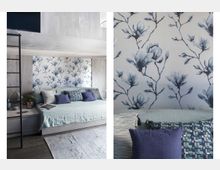 Wohnzimmer mit moderner Einrichtung, einer hellblauen Couch, blauen Kissen und einer Akzentwand mit floraler Tapete in Blau-Weiß-Tönen. Links daneben ein schlichter Nachttisch mit Dekoration und eine schwarze Leiter, die zu einer oberen Ebene führt.