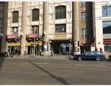 Straßenansicht des historischen Admiralspalasts in Berlin, mit verzierten Fassadenelementen und hohen Fenstern. Im Erdgeschoss befinden sich Geschäfte und Restaurants sowie ein Durchgang zur inneren Hofpassage.