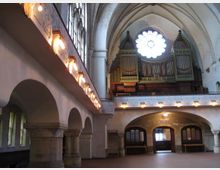 Innenraum einer historischen Kirche mit gotischen Gewölbedecken. Im Hintergrund steht eine große Orgel unter einem runden Rosettenfenster, während an den Seiten Arkaden und verziertes Mauerwerk zu sehen sind.