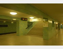 U-Bahn-Station mit türkisfarbenen Kacheln an den Wänden, einer Treppe, die nach oben führt, und einem Schild mit der Aufschrift "U2 Ruhleben ↔ Pankow". Eine digitale Anzeigetafel zeigt Abfahrtszeiten, und der Bahnsteig ist mit Deckenlampen beleuchtet.