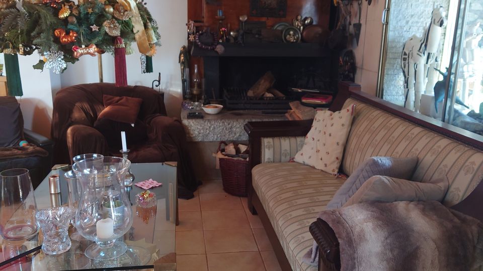 Gemütliches Wohnzimmer mit einer Sitzecke, bestehend aus einem gepolsterten Sofa und Sesseln, einem Kamin in einer dunklen Wandnische und einem Glastisch mit Kerzen. Die Dekoration umfasst weihnachtlichen Schmuck und Holzdetails, die den rustikalen Stil unterstreichen.