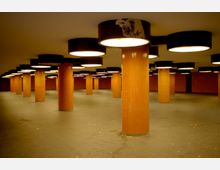 Unterirdischer Durchgang mit orange gefliesten, runden Säulen, die große runde Deckenleuchten tragen. Der Boden ist dunkel, die Wände und Säulenpfeiler sind ebenfalls in orange gehalten.