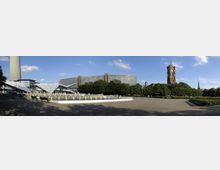 Weitläufiger Platz mit einem flachen Brunnen in der Mitte, umgeben von Bäumen und modernen Gebäuden. Im Hintergrund sind der rote Backsteinturm des Berliner Rathauses und der Fernsehturm sichtbar.