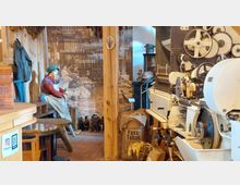 Ausstellungsraum in einem Museum mit historischen Gegenständen, darunter eine Tabakverarbeitungsmaschine, ein Fass mit getrocknetem Tabak und eine bekleidete Schaufensterpuppe. Im Hintergrund sind Holzelemente, getrocknete Tabakblätter und eine Wand mit alten Tabakanbaubildern zu sehen.