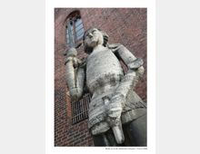 Steinfigur eines mittelalterlichen Ritters mit Schwert, aufgenommen vor einer Backsteinfassade mit Spitzbogenfenster und vergittertem Bereich, vermutlich Teil des Märkischen Museums in Berlin.