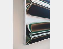 Nahaufnahme eines gerahmten abstrakten Kunstwerks mit metallischen, fließenden Linien in Grün-, Braun- und Silbertönen, das an einer hellen, glatten Wand hängt. Der Rahmen ist schlicht und aus gebürstetem Metall.