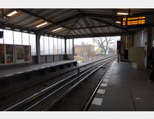 Bahnhof mit überdachtem Bahnsteig, Gleisen und einer Glaswand auf der linken Seite. An der Decke sind Lichter angebracht, und ein Anzeigebildschirm zeigt die Linien U1 und U3 mit Ziel "Warschauer Straße" an.