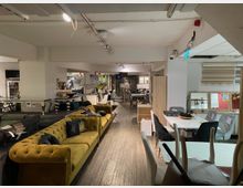 Ein geräumiger Möbel-Showroom mit einer Vielzahl von ausgestellten Sofas, Stühlen und Tischen in verschiedenen Designs. Die Einrichtung umfasst helle Beleuchtung, dekorative Elemente und Regale mit zusätzlichen Produkten im Hintergrund.