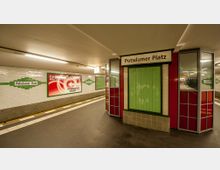 U-Bahn-Station Potsdamer Platz in Berlin mit weißen Kacheln an den Wänden, grünem Dekor und einem Bahnsteig mit gelben Sicherheitslinien. Ein Kiosk mit grünen und roten Elementen steht im Vordergrund, und Werbeplakate sowie Stationsschilder sind sichtbar.