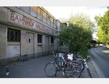 Außenansicht der U-Bahn-Station "Bahnhof Hallesches Tor" in Berlin, mit einem historischen Schriftzug an der Sandsteinfassade. Im Vordergrund stehen geparkte Fahrräder, daneben verläuft eine Baum gesäumte Straße.