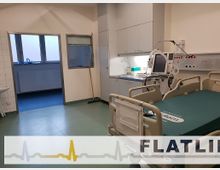 Ein Krankenhauszimmer mit einem Krankenhausbett, einem Monitor zur Patientenüberwachung und medizinischer Ausrüstung an der Wand. Im Hintergrund befinden sich ein Waschbereich und ein Durchgang zu einem Nebenraum.