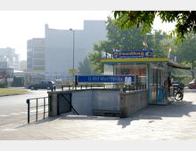 Eingang zur U-Bahn-Station „Moritzplatz“ mit einem blauen Schild und Treppen, daneben ein Imbisspavillon mit der Aufschrift „Foodbag“. Im Hintergrund sind Autos, Gebäude und Bäume zu sehen.