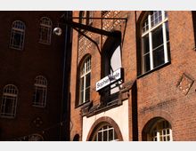 Backsteinfassade eines mehrstöckigen Gebäudes mit hohen, bogenförmigen Sprossenfenstern und dekorativen Mauerwerksmustern. An einem Metallausleger hängt ein Schild mit der Aufschrift „Sophiensæle“ über einem Eingang.