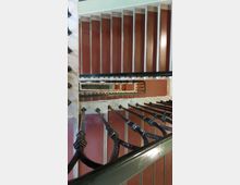 Treppenhaus mit mehrstöckigem, rechteckigem Treppenlauf, charakterisiert durch weiße Stufen, rote Wände und schwarze Metallgeländer. Die Treppen sind aus einer vertikalen Perspektive nach unten zu sehen.