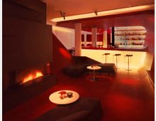 Eine stilvolle Lounge mit warmem roten Licht, modernen Möbeln und einem Kamin auf der linken Seite. Im Hintergrund befindet sich eine beleuchtete Bar mit hohen Stühlen und zahlreichen Flaschen im Regal.