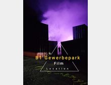 Eine nächtliche Szene in einem Gewerbepark mit zwei großen, dunklen Versandcontainern im Vordergrund. Im Hintergrund ist eine Person als Silhouette vor intensiv violett beleuchtetem Nebel sichtbar.