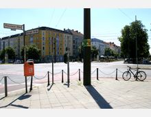 Straßenkreuzung in einer städtischen Umgebung mit Wohngebäuden im Hintergrund. Zu sehen sind Straßenschilder der Kreuzung „Prenzlauer Allee“ und „Danziger Straße“, ein parkendes Fahrrad, eine orange Mülltonne und Oberleitungen für den öffentlichen Verkehr.