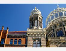 Detailaufnahme einer Synagoge mit einer Kuppel im maurischen Baustil. Die Fassade besteht aus Ziegelmauerwerk und kunstvollen Verzierungen, die Kuppel ist mit goldenen Details geschmückt, vor klarem, blauem Himmel.
