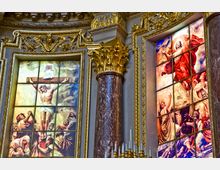 Buntglasfenster in einer Kirche mit religiösen Szenen: links die Kreuzigung Jesu und rechts die Auferstehung. Die Szenerie ist von goldverzierter Architektur mit Marmorsäulen umrahmt.