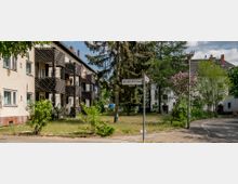 Wohngebäude in einer Wohnsiedlung mit Balkonen aus Holz, umgeben von Bäumen, Sträuchern und einer Rasenfläche. Im Vordergrund steht ein Straßenschild mit der Aufschrift „Nordlichtstraße“.