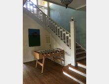 Treppenhaus mit Holzstufen und weißem Geländer, daneben ein Tischkicker auf einem Holzfußboden. An der Wand befindet sich eine kleine dekorative Wandinstallation.