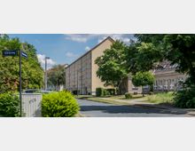 Wohngebiet mit mehrstöckigen Wohngebäuden und einem niedrigeren Gebäude mit Flachdach auf der rechten Seite. Der Bereich ist von Bäumen, Grünflächen und einer asphaltierten Straße umgeben; Straßenschilder "Eichenweg" und "Kastanienweg" sind sichtbar.