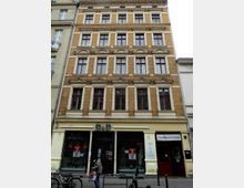 Fassade eines mehrstöckigen Altbaus mit gelblichen Klinkersteinen und verzierten Fensterrahmen. Im Erdgeschoss befinden sich ein Geschäft mit dem Schild "D&D" und der Eingang zum Puppen-Theater-Museum.