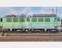 Grüne Elektrolokomotive der Eisenbahngesellschaft Potsdam (EGP) mit gelbem und rotem Streifen, geparkt auf einem Gleisabschnitt. Im Hintergrund bewölkter Himmel und ein Teil eines Lichtmastes sichtbar.