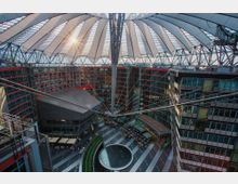 Überdachter Innenhof des Sony Centers in Berlin mit futuristischer Zeltdachkonstruktion und umliegenden modernen Glasgebäuden; im Zentrum ein Brunnen und Sitzbereiche mit Cafés und Restaurants.