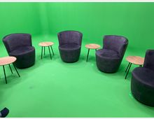 Vier lila Sessel und vier runde Beistelltische mit Holzplatten stehen in einem Raum mit grünem Hintergrund und grünem Boden, der als Greenscreen-Studio genutzt werden kann.