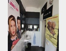 Kleines Badezimmer mit weiß gefliesten Wänden, einem Waschbecken an der linken Seite und einem Spiegel darüber. An den Wänden hängen Kinoplakate, darunter eines von "Bridget Jones’ Baby" und ein gelbes von "Papillon".