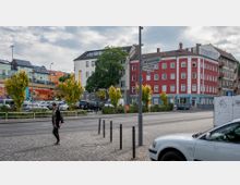 Straßenszene in einer städtischen Umgebung mit Wohngebäuden, darunter ein auffälliges rotes Gebäude mit weißen Fensterrahmen. Im Vordergrund eine Straße mit Bäumen auf einem Grünstreifen, geparkten Autos und einem Straßenschild mit den Namen „Wönnichstraße“ und „Einbecker Straße“.