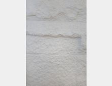 Weiße, raue Steinoberfläche mit horizontal verlaufenden Fugen, die die Blöcke klar voneinander abgrenzen. Die Textur zeigt unregelmäßige Erhebungen und Vertiefungen.