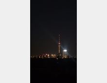 Nachtszene einer Stadt mit dem beleuchteten Berliner Fernsehturm im Zentrum, umgeben von weiteren erleuchteten Gebäuden und einem dunklen Himmel im Hintergrund.