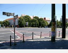 Straßenkreuzung in einer städtischen Umgebung, mit Schildern der "Danziger Straße" und "Prenzlauer Allee". Im Hintergrund sind mehrstöckige Gebäude mit roten Dächern und Bäume zu sehen, während Straßenbahndrähte die Szene überspannen.