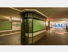 U-Bahn-Station mit grün-weiß gekachelten Wänden und einem gusseisernen Stützpfeiler in grünem Farbton. Ein Schild mit der Aufschrift „Potsdamer Platz“ ist an einer der Wände angebracht, im Hintergrund führen Treppen nach draußen.
