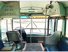 Innenraum eines alten Linienbusses mit Blick auf den Fahrersitz und das Armaturenbrett. Die Sitzpolster und Wände sind in Grün- und Blautönen gehalten, und vorn sind Schilder zu sehen, darunter eines mit der Aufschrift „No smoking“.