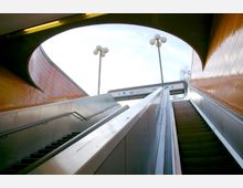 Treppenaufgang und Rolltreppe an einem U-Bahnhof mit orangefarbenen Fliesenwänden und einem halbovalen Dachauschnitt. Im Hintergrund sind Beschilderungen zum ZOB (Zentraler Omnibusbahnhof) und zwei Straßenlaternen sichtbar.