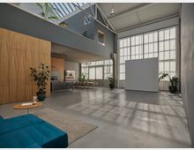 Moderner, minimalistisch eingerichteter Innenraum mit hohen Decken und großen Fenstern, die durchsichtige Vorhänge tragen. Der Raum umfasst eine offene Küche mit hellen Holzelementen, eine Sitzecke mit einem blauen Sofa, einen großen freien Bodenbereich und Pflanzen als Akzente.