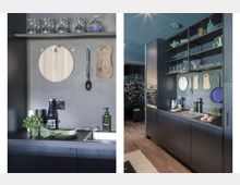 Moderne Küchenzeile in dunklem Design mit mattschwarzen Oberflächen, einem Edelstahlwaschbecken und offenen Regalen mit Gläsern und Flaschen. An der Rückwand hängen Schneidebretter und Küchenutensilien, während frische Zutaten und Kräuter auf der Arbeitsfläche liegen.